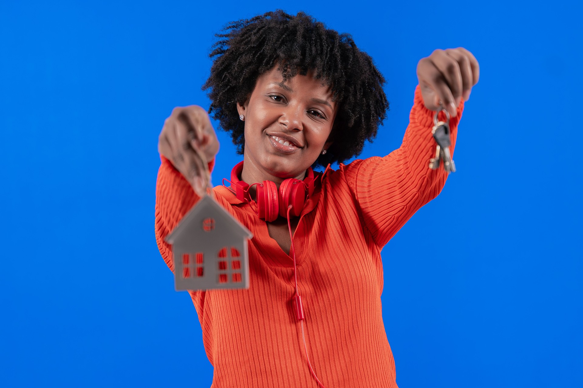Mujer afroamericana sosteniendo las llaves de la casa y el modelo de la casa, sonriendo con confianza