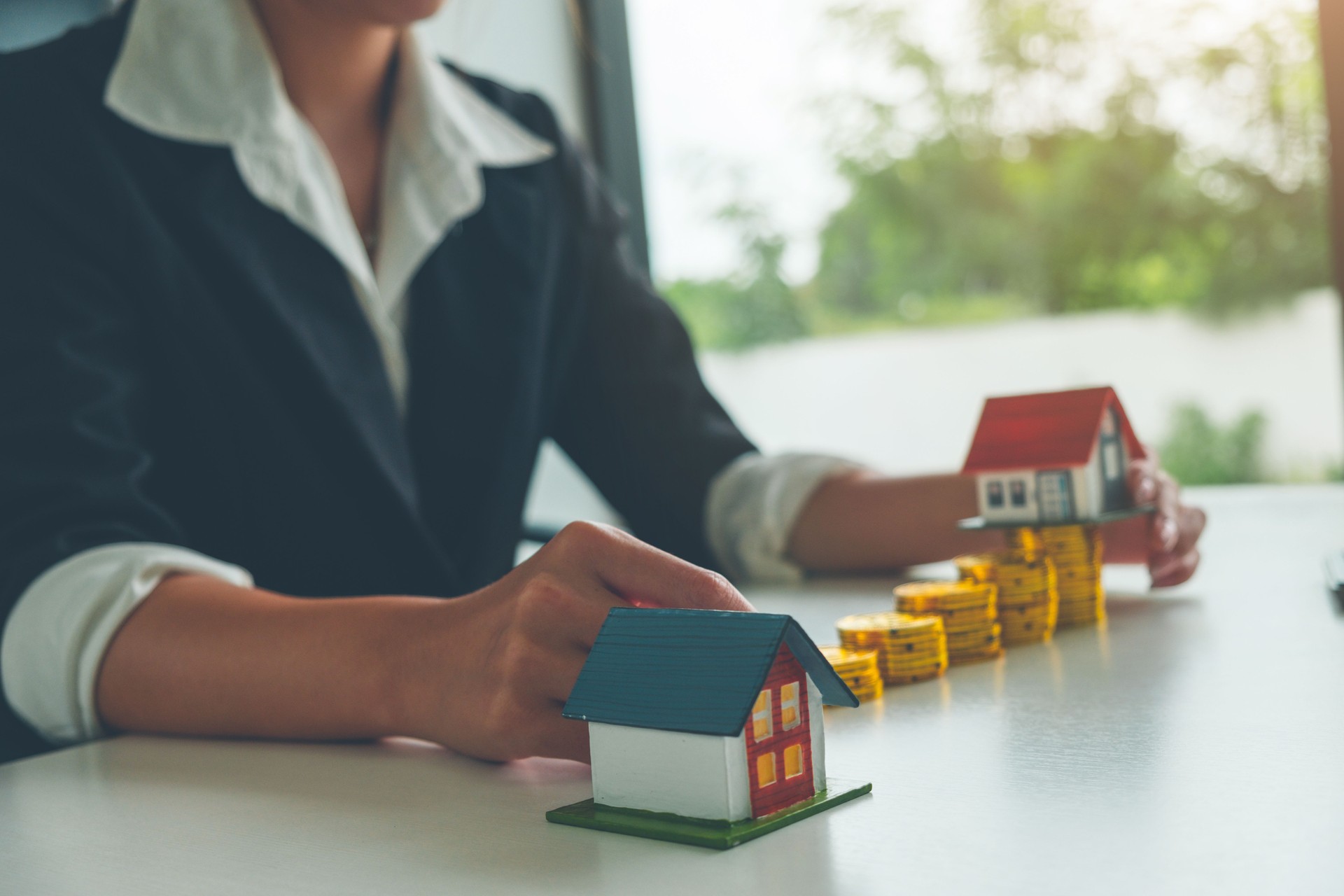 Agente inmobiliario las mujeres mantener un modelo de casa pequeña en su mano y pila de moneda de oro, concepto inmobiliario